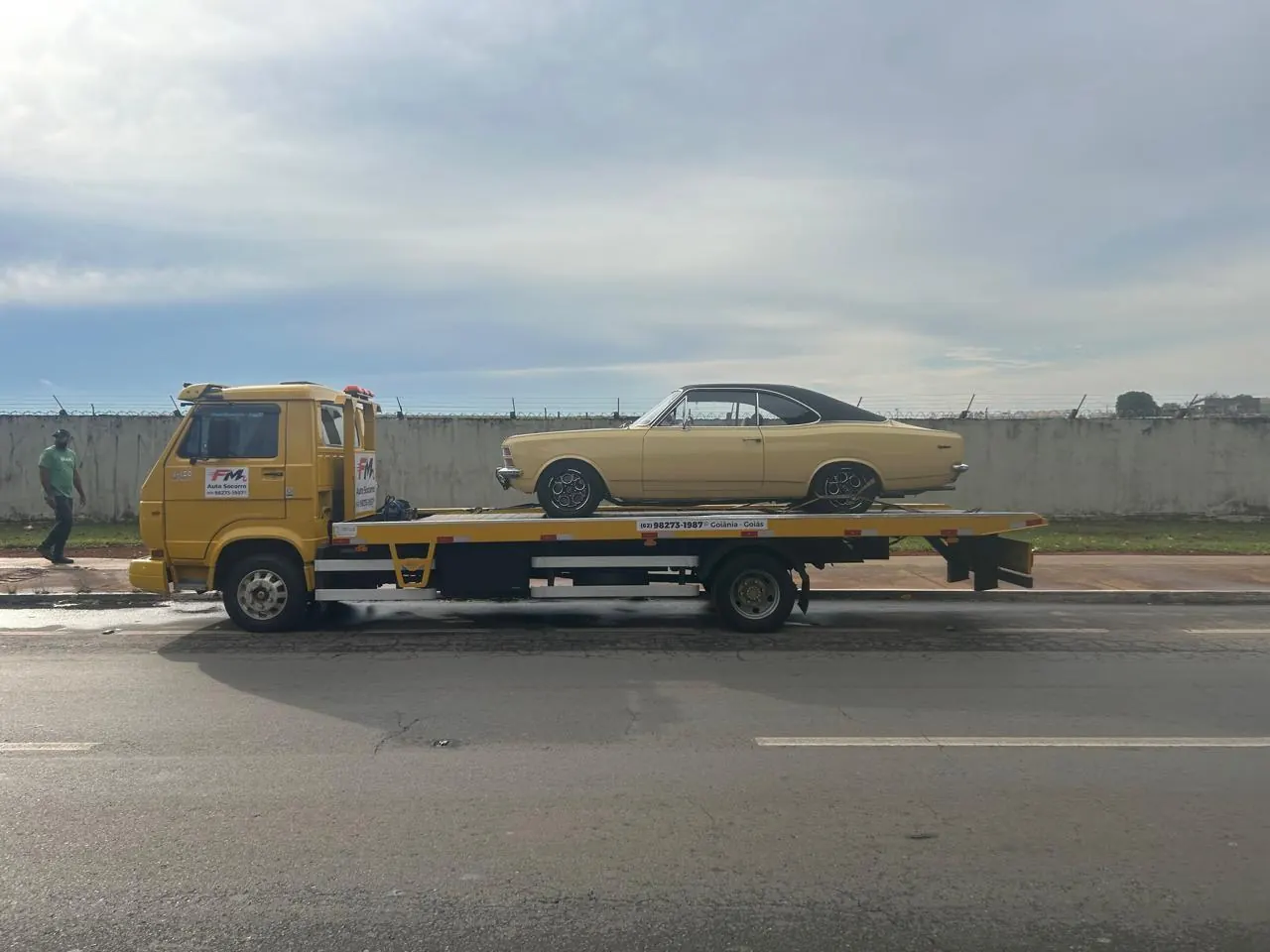 Guincho plataforma da FM Auto Socorro levando um Chevrolet Opala clássico amarelo, visto de lado em uma avenida